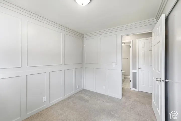 Neutral-toned carpeting, decorative wainscoting paneling, crown molding, and a flush-mount ceiling light fixture