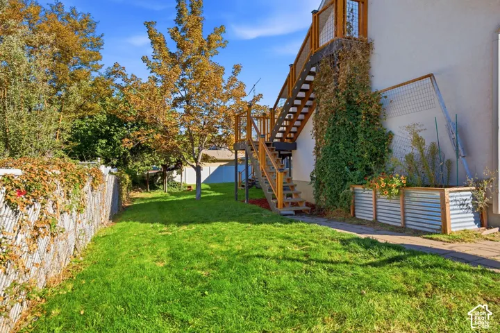 Expansive green lawn with a chain-link fence, mature trees, and a multi-level exterior staircase
