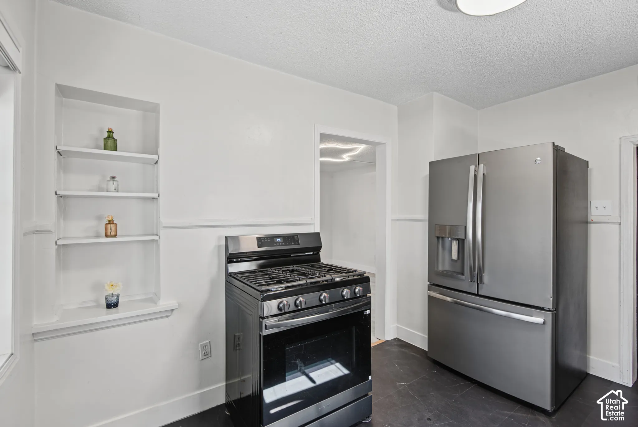 Stainless steel French door refrigerator, stainless steel gas range, built-in shelving, dark flooring, and white walls