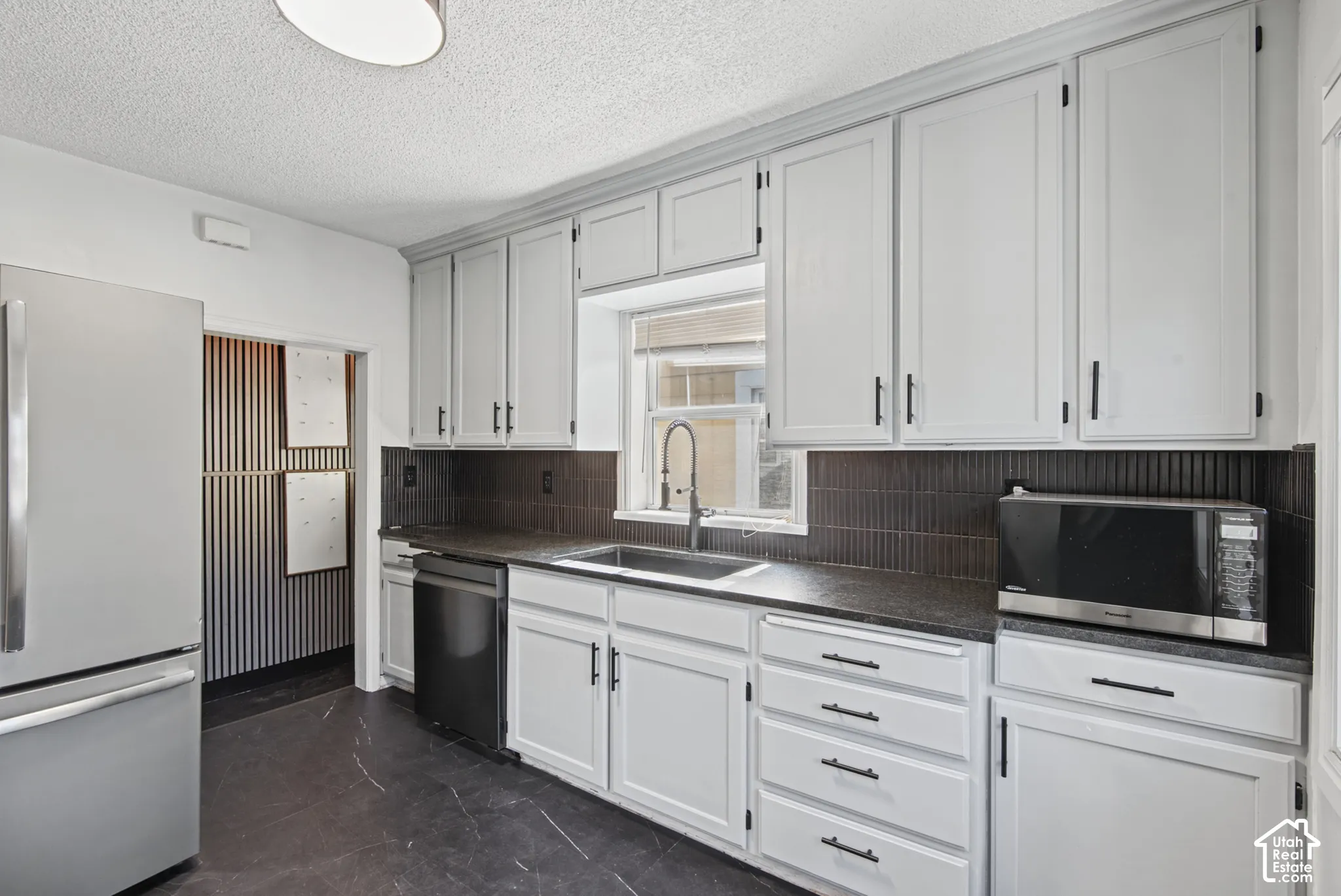 Kitchen featuring white cabinetry, dark countertops, a dark tile backsplash, a stainless steel refrigerator, and dark flooring