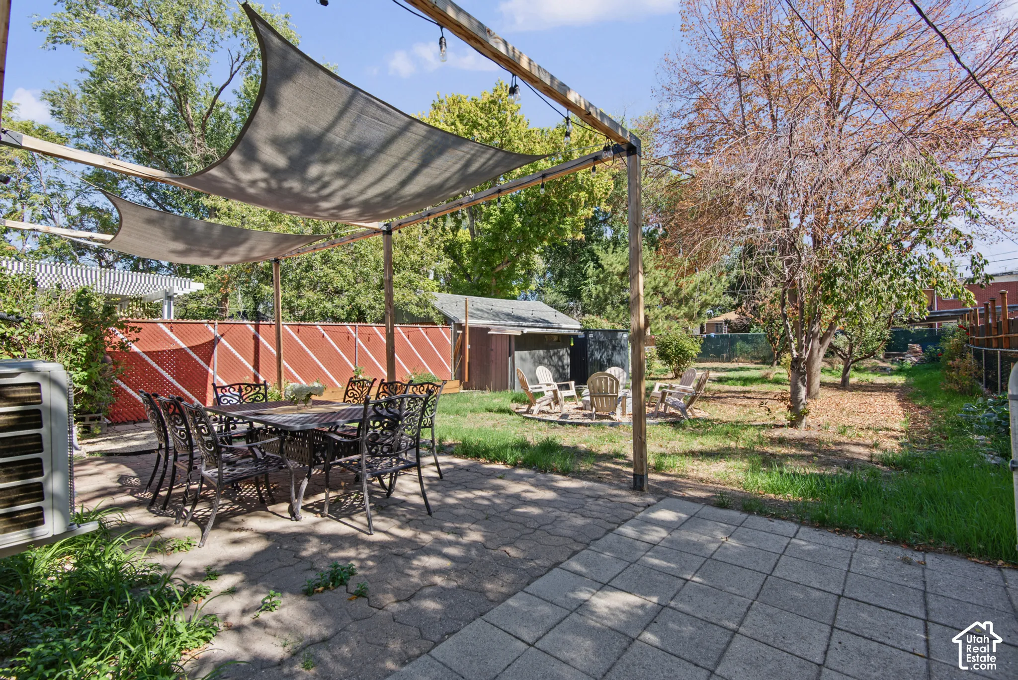 Paved patio area, overhead shade structure, wood privacy fence, and mature trees