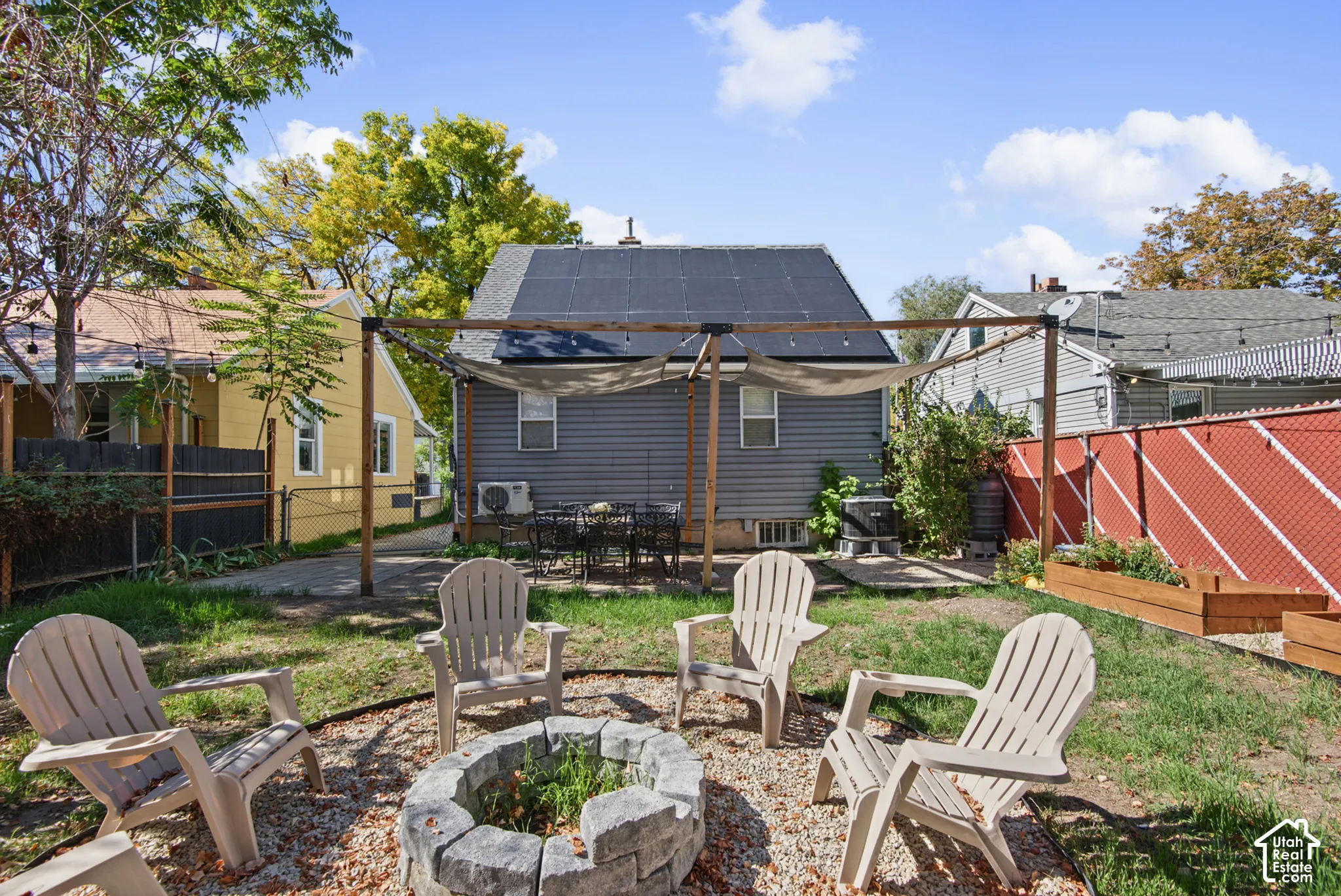 Backyard featuring a stone fire pit, wood pergola with shade fabric, raised garden beds, and a patio area