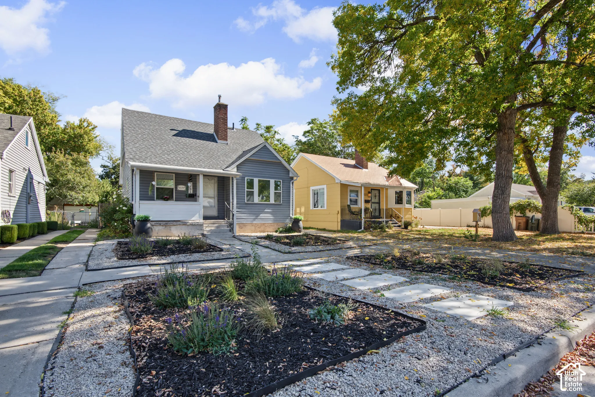 Gray siding exterior with white trim, covered front porch, prominent brick chimney, and concrete walkway