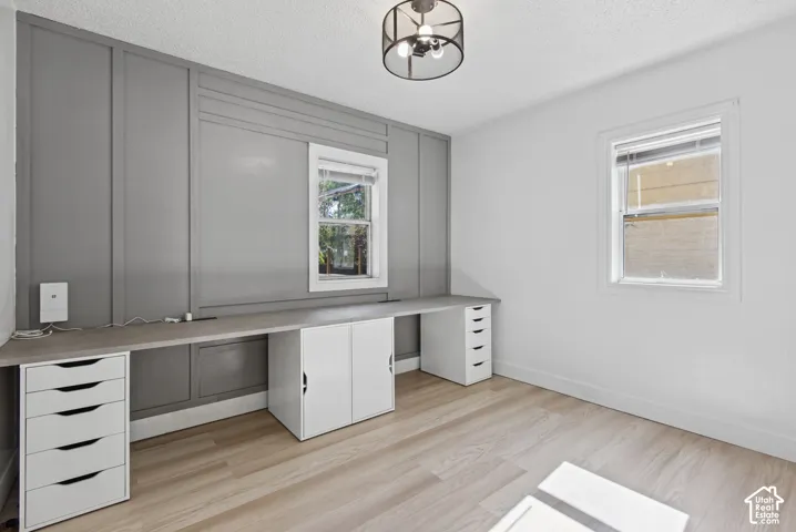 Panel accent wall, built-in desk with storage, wood-finish flooring, two windows, and a ceiling-mounted light fixture