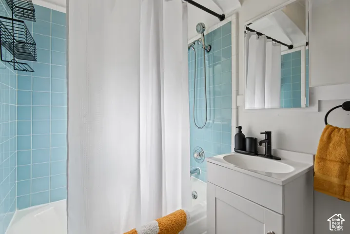 Bathtub with blue tiled surround, chrome showerhead, and white vanity with an integrated sink and matte black faucet