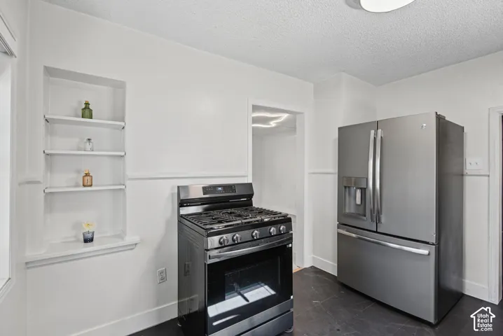 Stainless steel French door refrigerator, stainless steel gas range, built-in shelving, dark flooring, and white walls