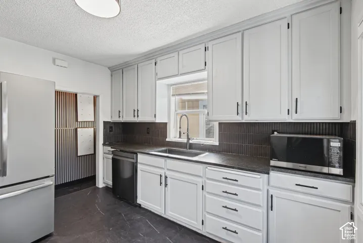 Kitchen featuring white cabinetry, dark countertops, a dark tile backsplash, a stainless steel refrigerator, and dark flooring
