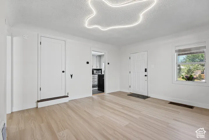 Hardwood-finish flooring, white walls, modern ceiling light fixture, white interior door, and a white exterior door