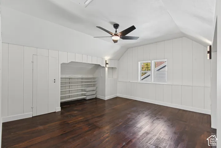 Hardwood flooring, painted paneling, built-in shelving, sconce lighting, and a ceiling fan with light fixture