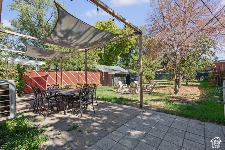 Paved patio area, overhead shade structure, wood privacy fence, and mature trees