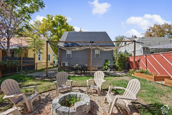 Backyard featuring a stone fire pit, wood pergola with shade fabric, raised garden beds, and a patio area