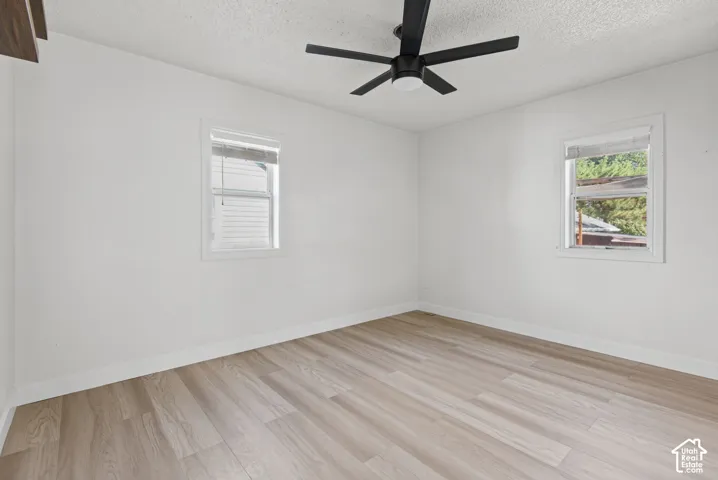 White walls with wood-finish flooring, two windows with white trim, and a black ceiling fan