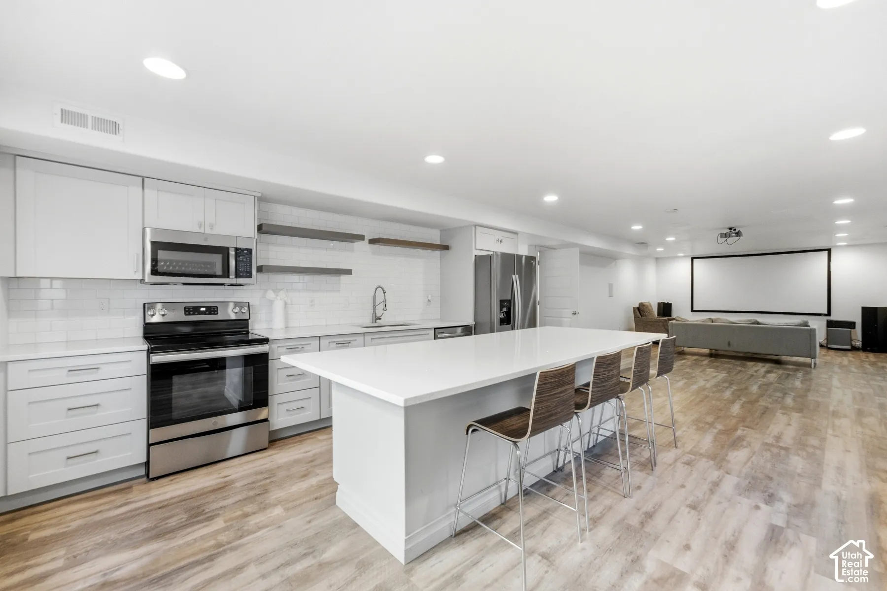 Full kitchen with stainless steel appliances, white subway tile backsplash, white countertops, and light wood-finish flooring