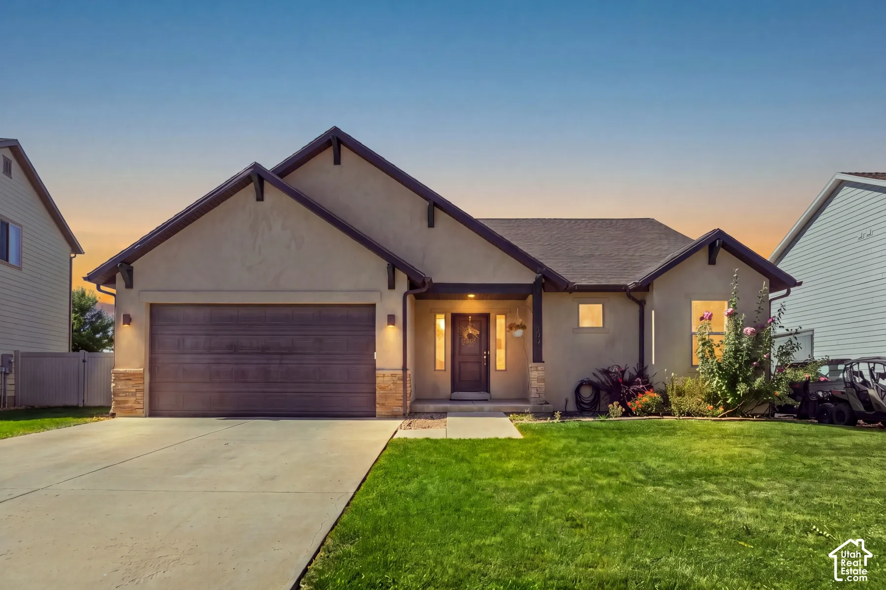 Stucco exterior with stone accents, attached two-car garage, covered entry, and manicured front lawn