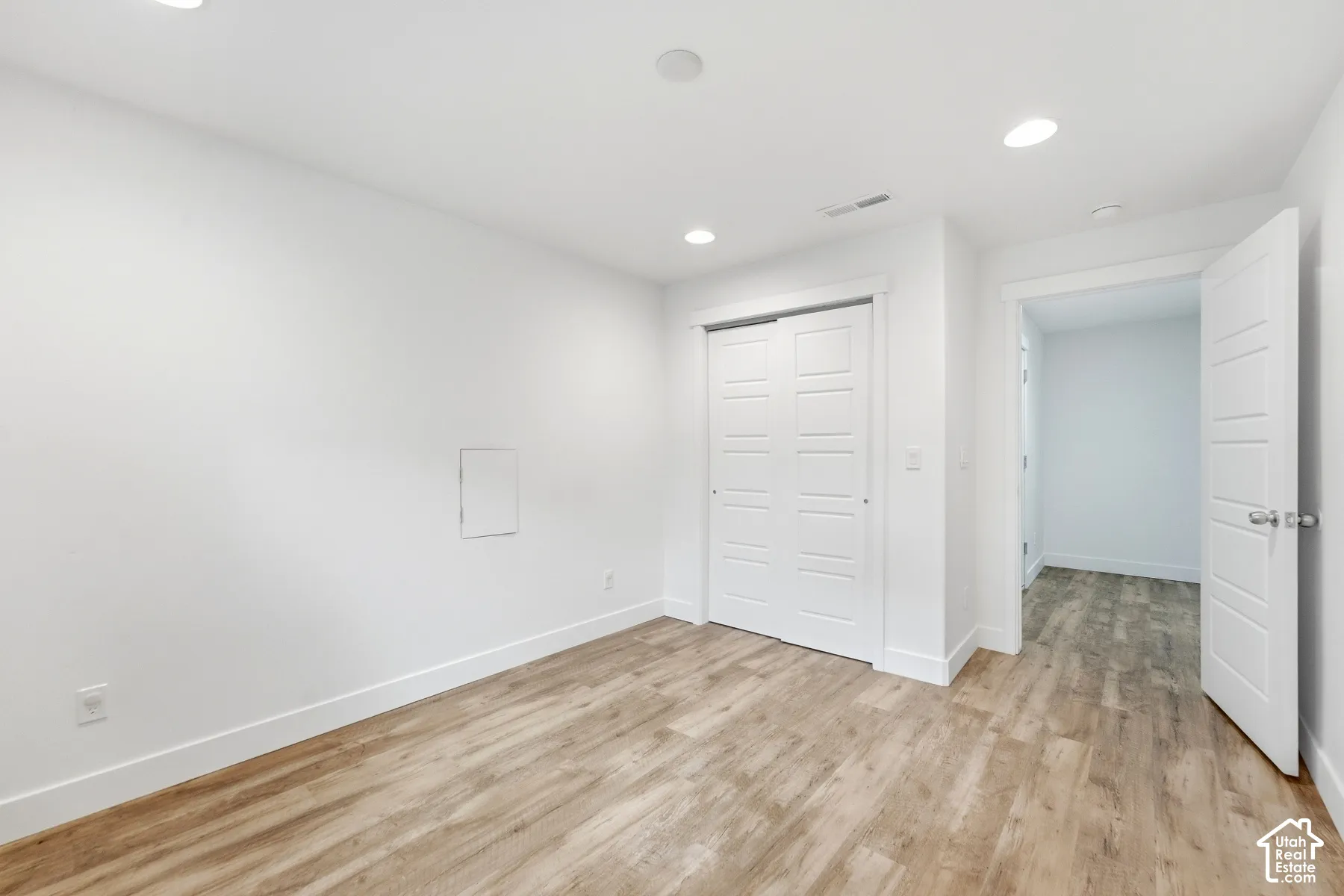 Recessed lighting with white trim, wood-finish flooring, white walls, white sliding closet doors, and a white interior door