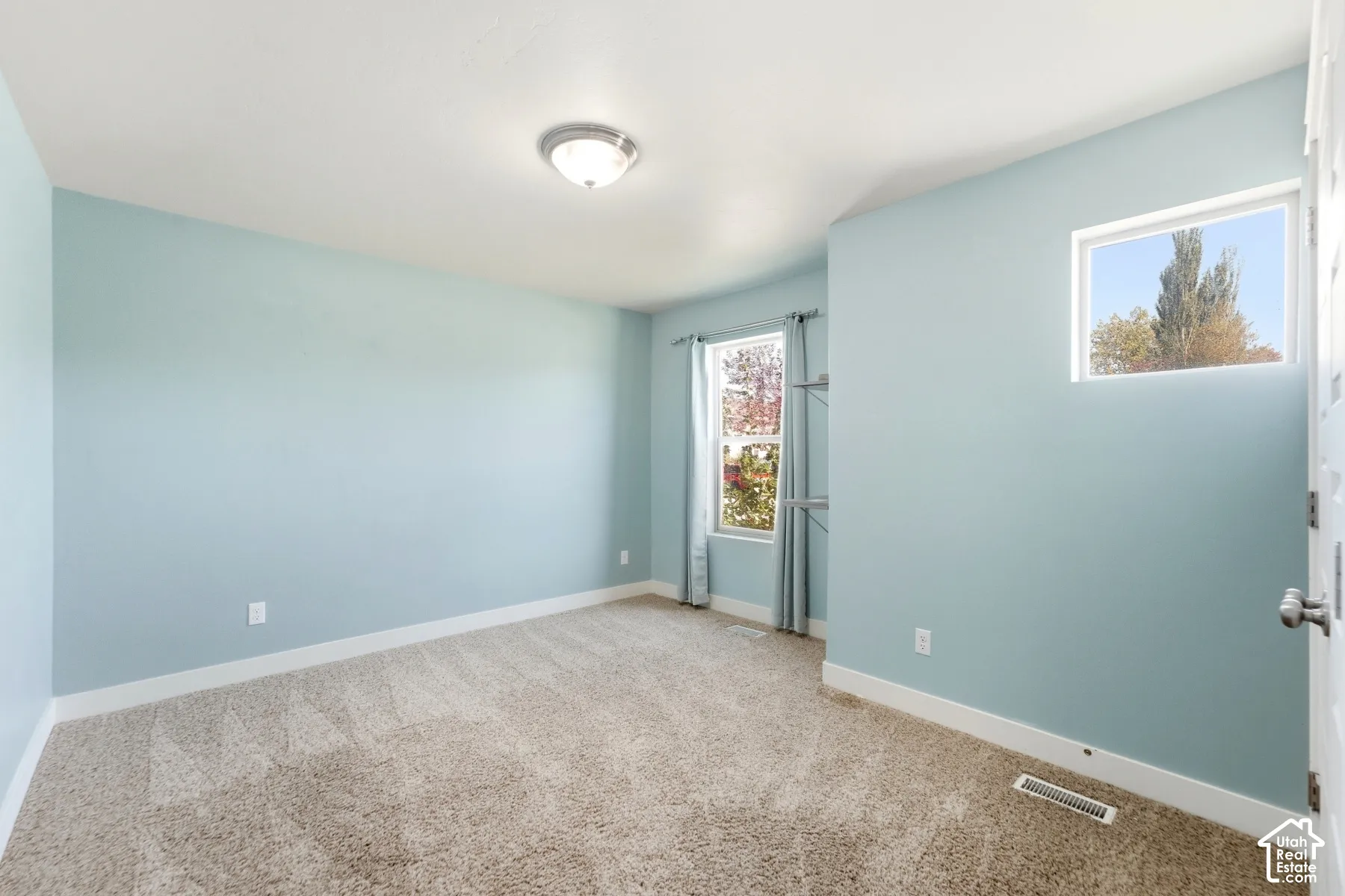 Carpet flooring, light blue wall paint, a window with curtains, a small window, and a ceiling light fixture