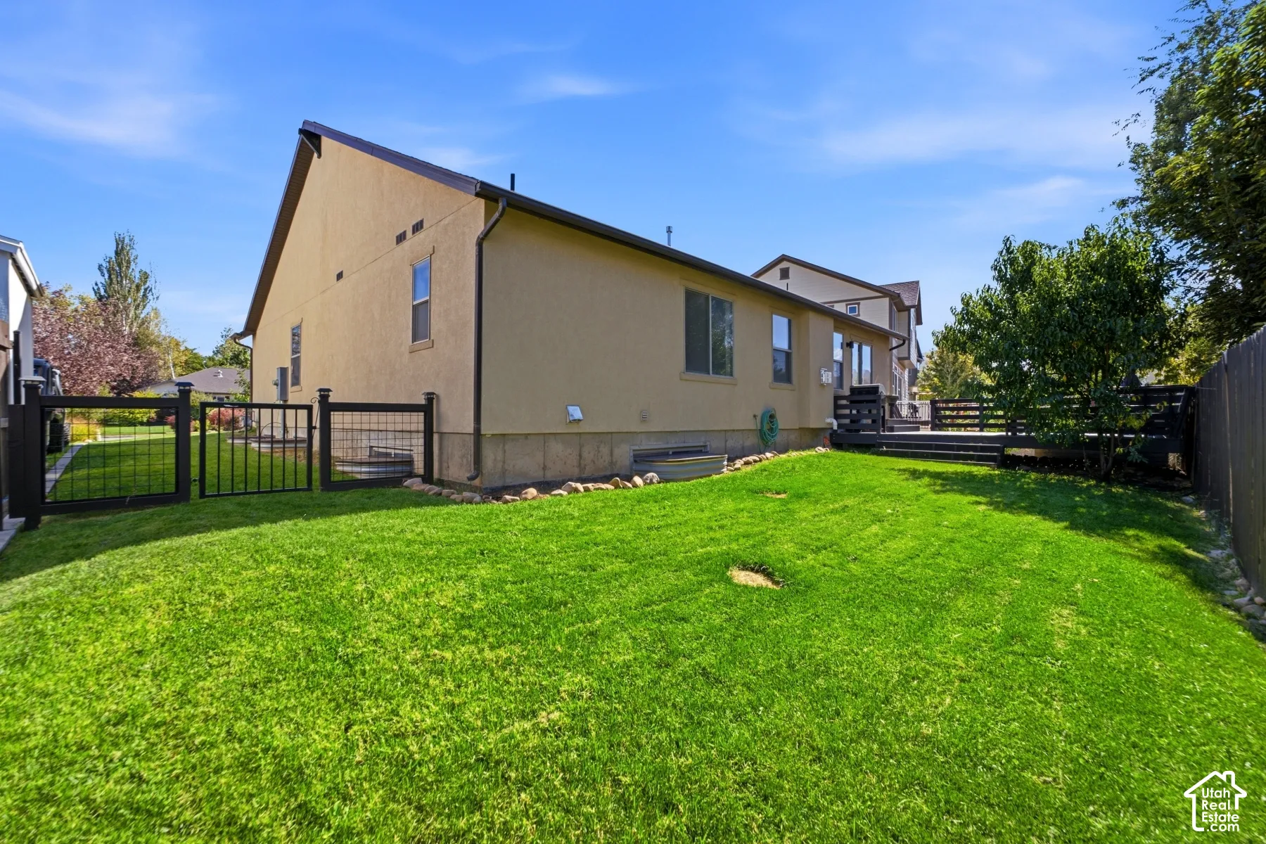 Expansive lawn area with a dark wood-finish deck, stucco exterior, and black metal fencing