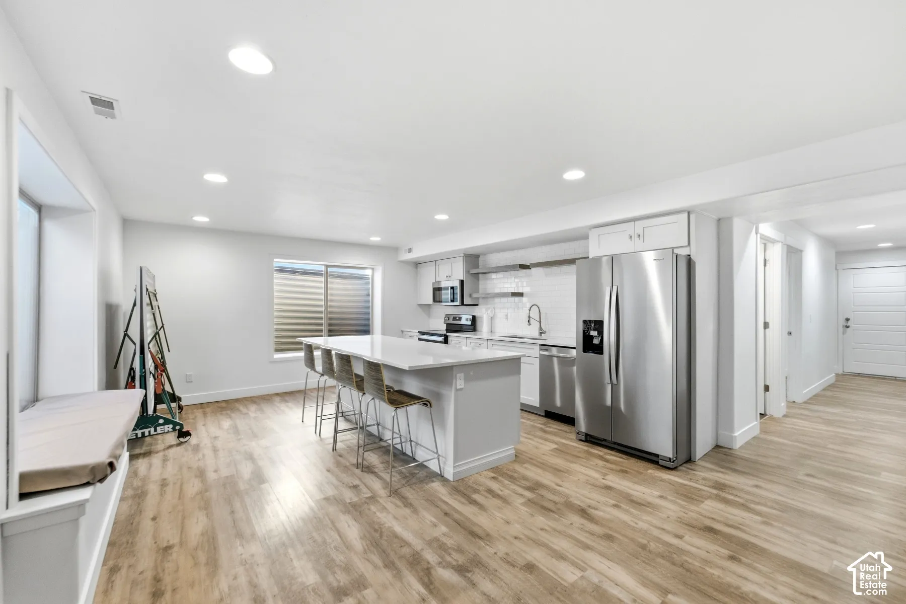 Open-concept kitchen with a large island, stainless steel appliances, light wood-finish flooring, and recessed lighting