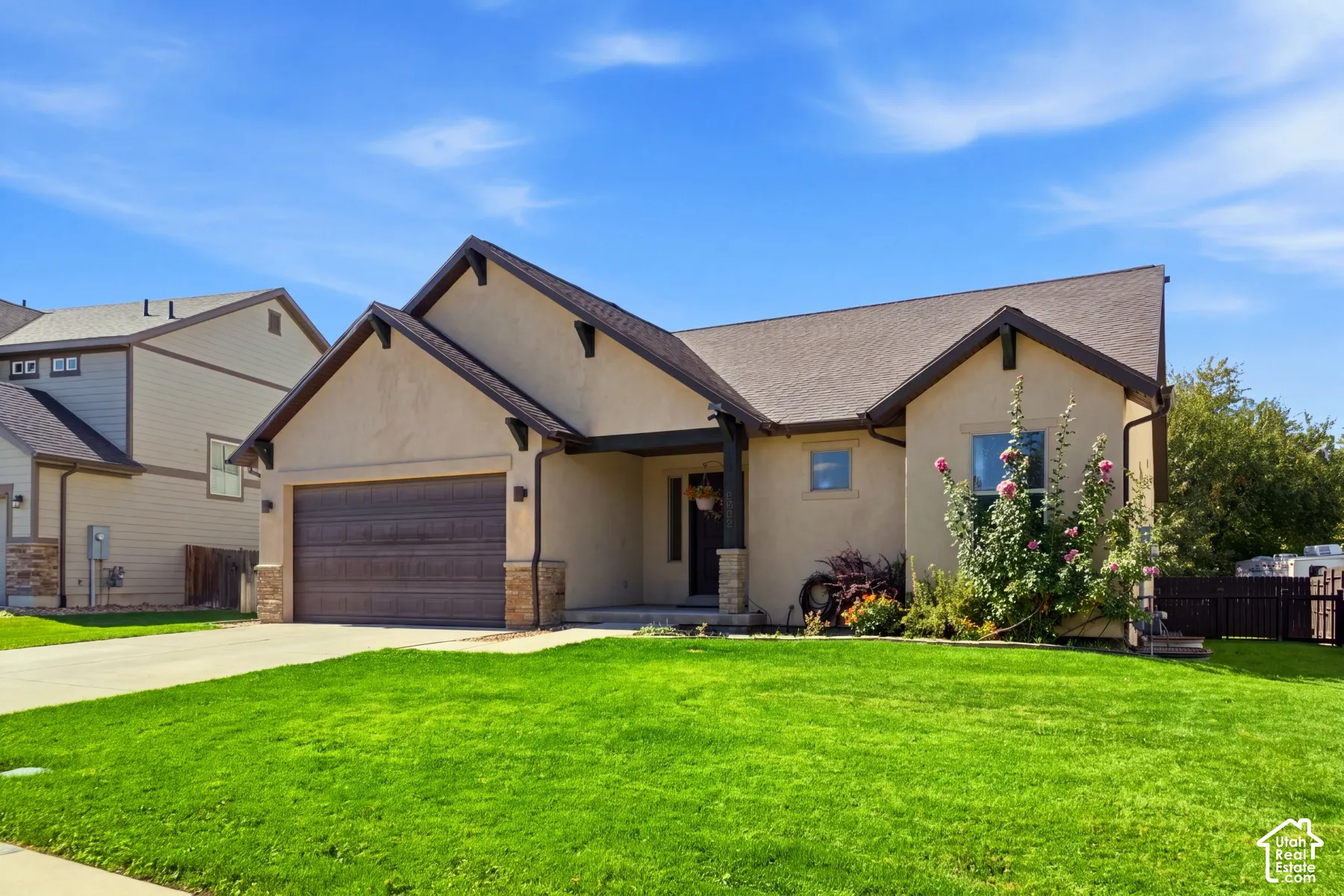 Stucco exterior with stone accents, attached garage, covered entry, and landscaped front yard