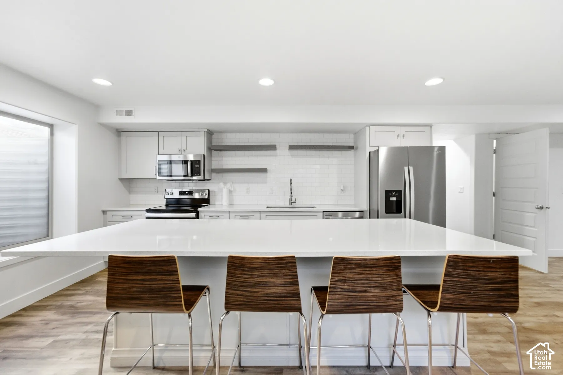 Modern kitchen featuring a large white island with seating, stainless steel appliances, light gray cabinetry, and subway tile backsplash