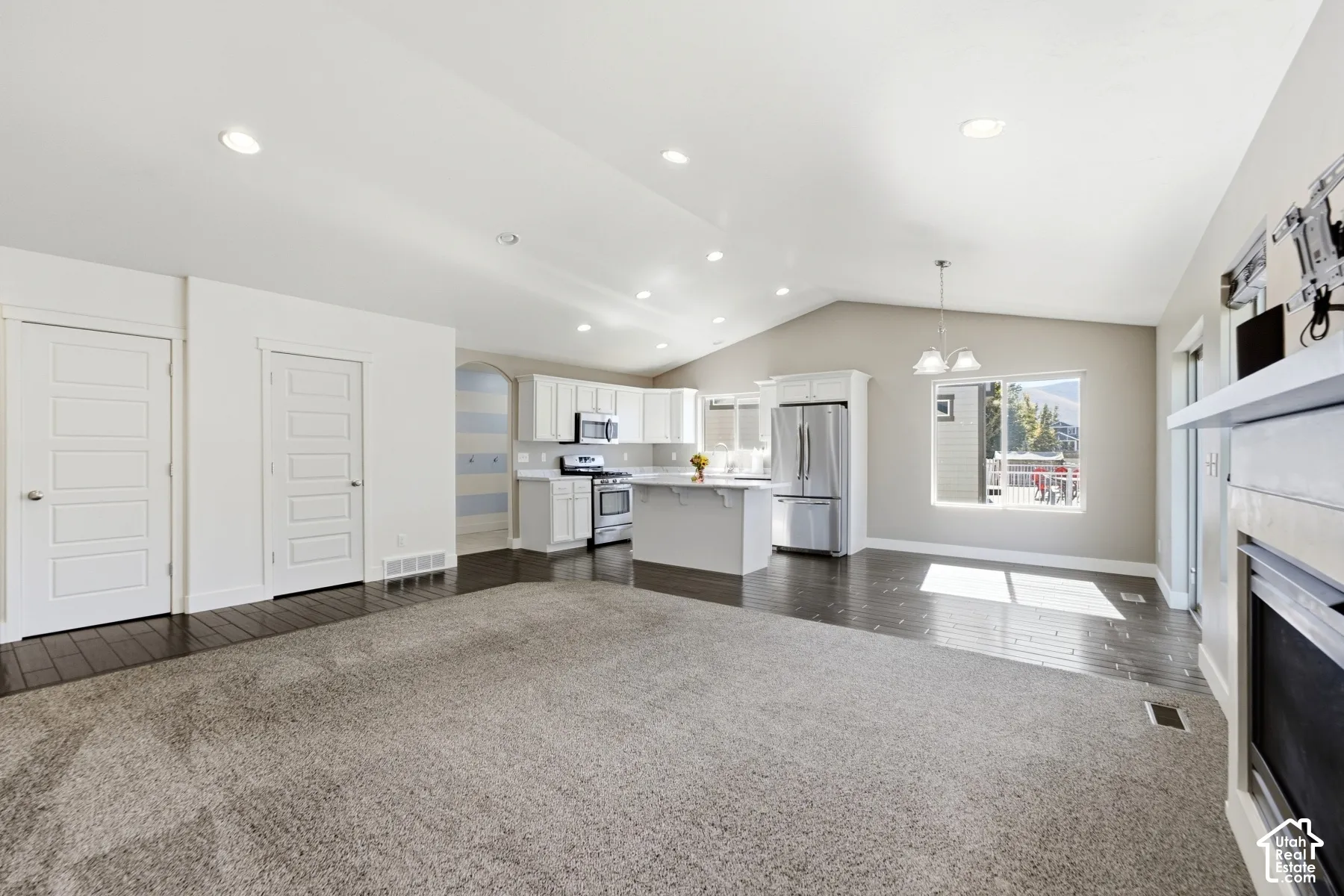 Vaulted ceilings, recessed lighting, wood-finish flooring, white cabinetry, and stainless steel appliances