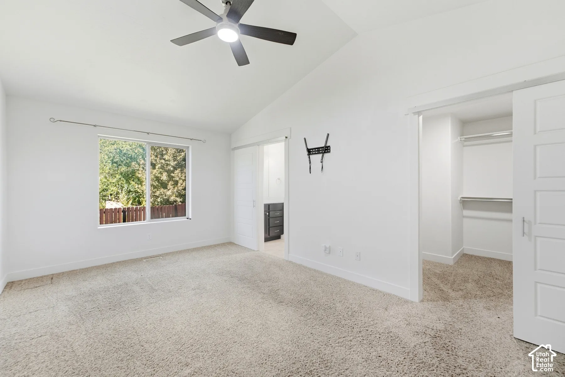 Vaulted ceiling with a ceiling fan, window with exterior greenery, carpeted flooring, and a barn door entry