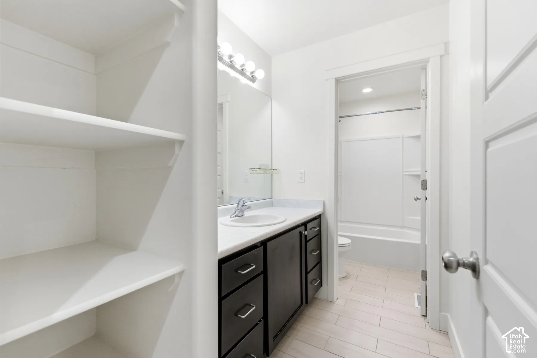 White built-in shelving, dark wood-finish vanity with a white countertop, and a vanity mirror with overhead lighting