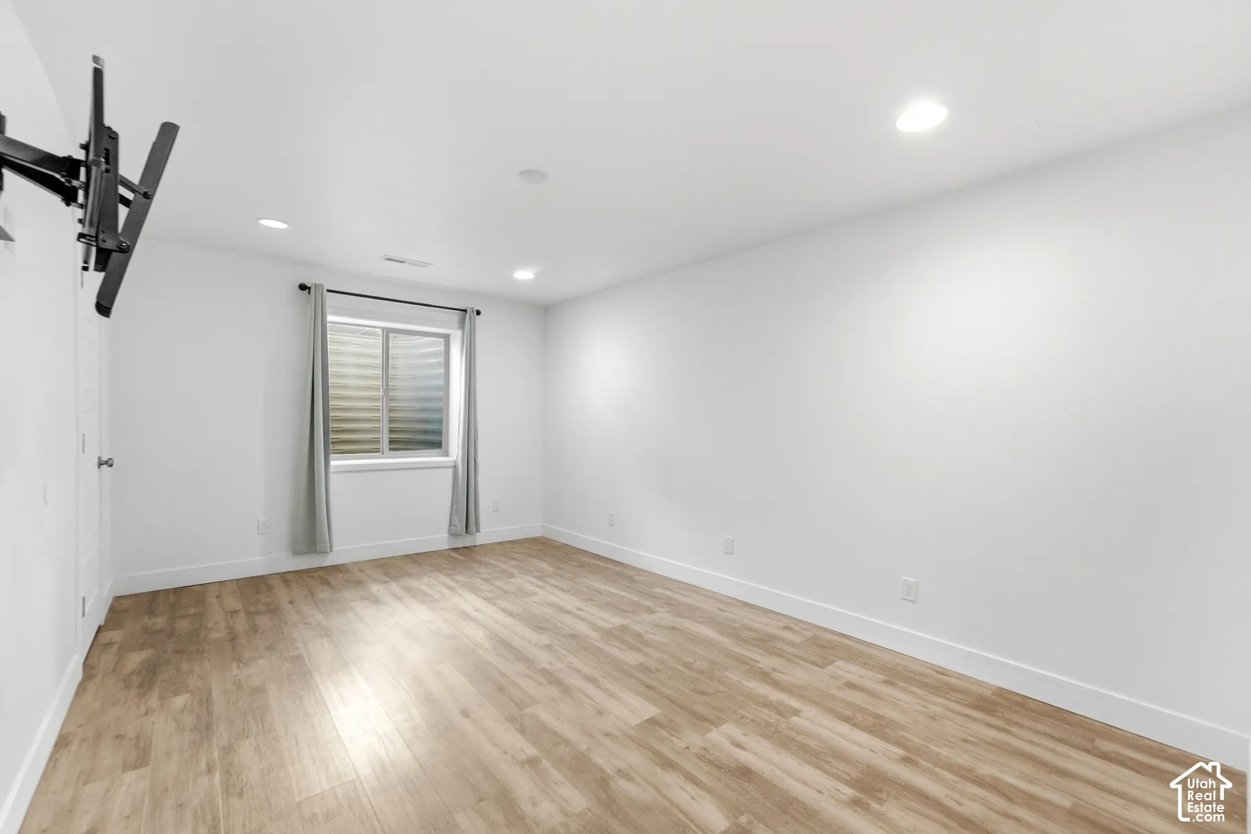 Recessed lighting illuminates the room, featuring wood-finish flooring and a window with blinds