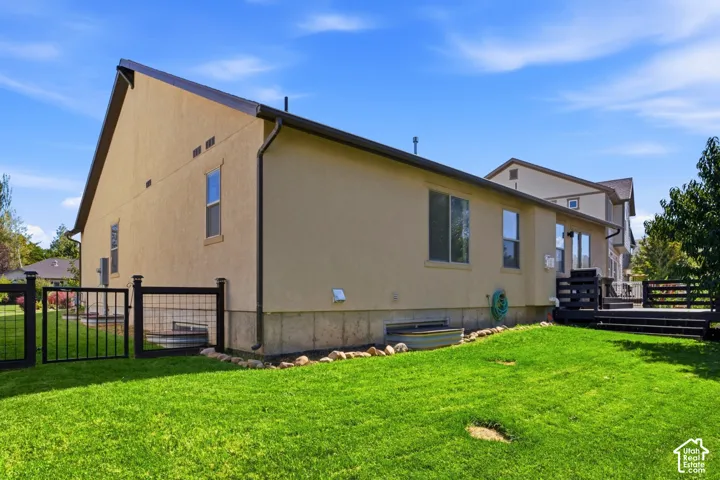 Expansive backyard featuring a manicured lawn, black fencing, a black deck, and a stucco exterior with multiple windows