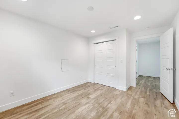 Recessed lighting with white trim, wood-finish flooring, white walls, white sliding closet doors, and a white interior door