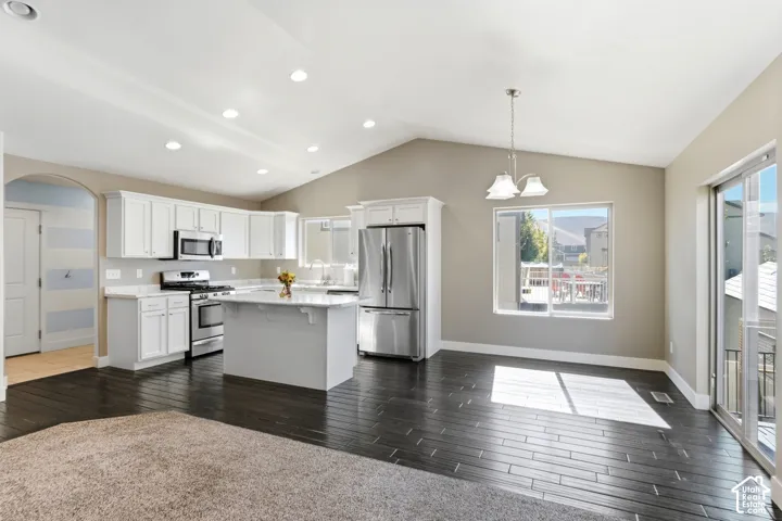 Kitchen featuring white cabinetry, stainless steel appliances, a center island with countertop, dark wood-finish flooring, and a vaulted ceiling