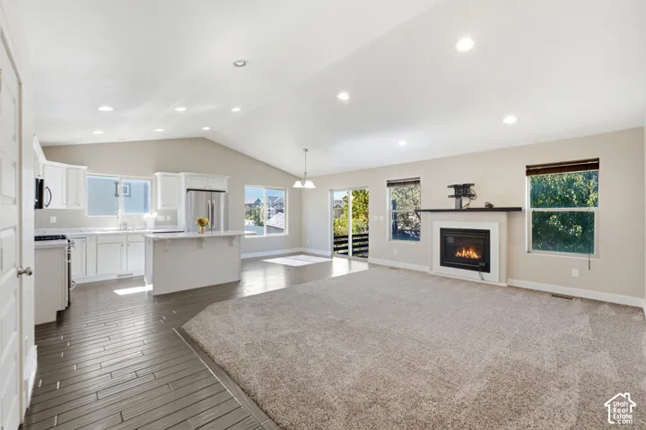 Open concept living space featuring vaulted ceilings, recessed lighting, a kitchen with white cabinetry and an island, a fireplace, and wood-finish flooring