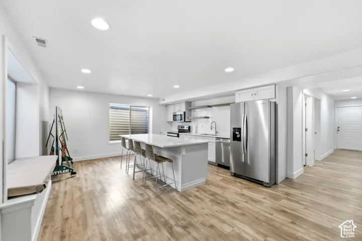 Open-concept kitchen with a large island, stainless steel appliances, light wood-finish flooring, and recessed lighting