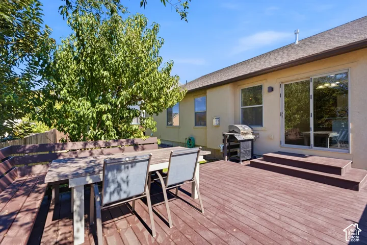 Expansive wood-finish deck with built-in seating, direct access to the interior via sliding glass doors, a stucco exterior, and mature landscaping