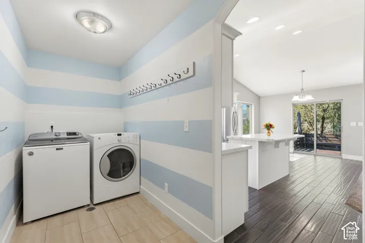Laundry area with tile flooring and wall-mounted hooks, opening to a kitchen with wood-finish flooring, a center island with a stone-finish countertop, and a sliding glass door