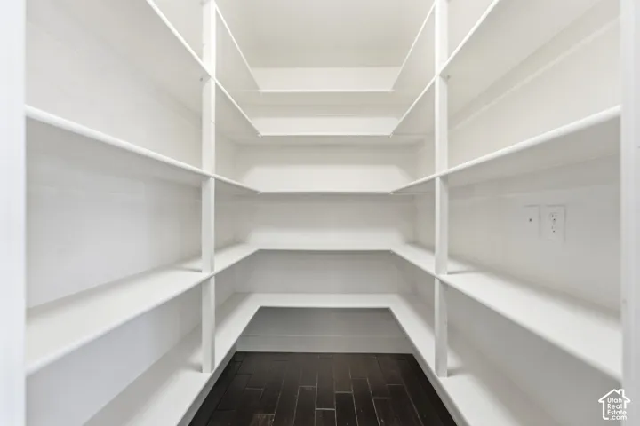 Expansive pantry featuring multi-level shelving, dark wood-finish flooring, and integrated electrical outlets