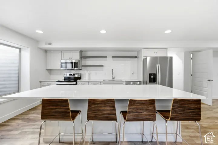 Modern kitchen featuring a large white island with seating, stainless steel appliances, light gray cabinetry, and subway tile backsplash