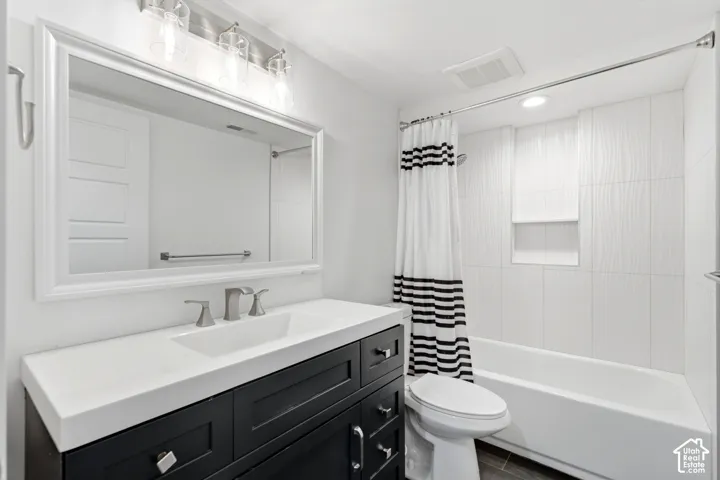 Black vanity with white countertop and integrated sink, framed mirror, three-light vanity fixture, tiled shower surround with recessed niche, and white bathtub