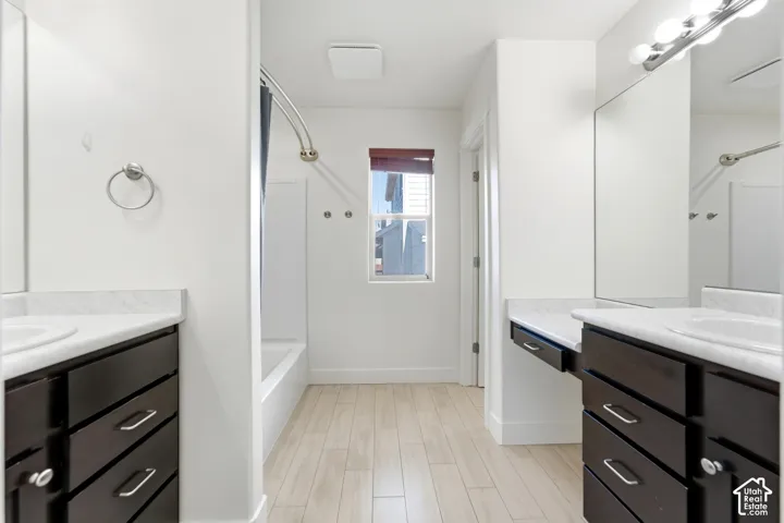 Dual vanity bathroom featuring black cabinetry with polished chrome hardware, white marble-finish countertops, large framed mirrors with integrated lighting, white subway tile walls, and wood-finish flooring