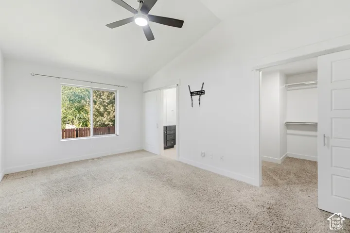Vaulted ceiling with a ceiling fan, window with exterior greenery, carpeted flooring, and a barn door entry