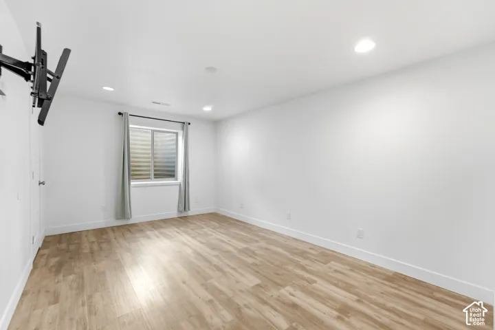 Recessed lighting illuminates the room, featuring wood-finish flooring and a window with blinds