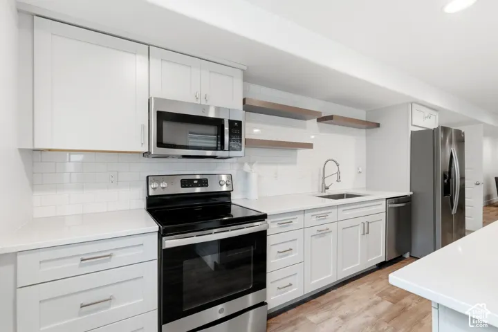 Modern kitchen featuring stainless steel appliances, white cabinetry, quartz countertops, a subway tile backsplash, and wood-finish flooring