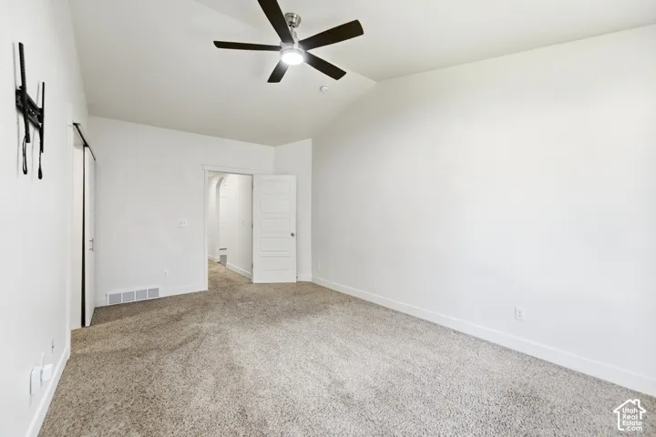 Vaulted ceiling with an attached ceiling fan, neutral carpeting, and white walls