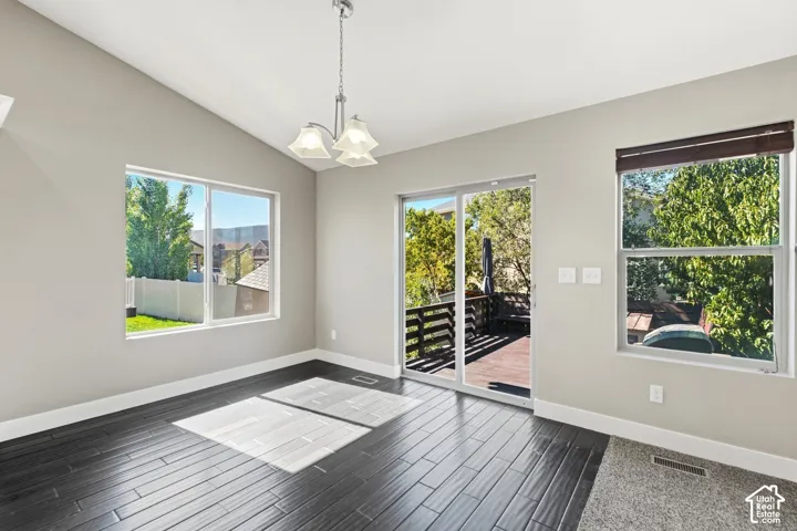 Vaulted ceiling, dark wood-finish flooring, sliding glass door to an outdoor deck, and multiple windows