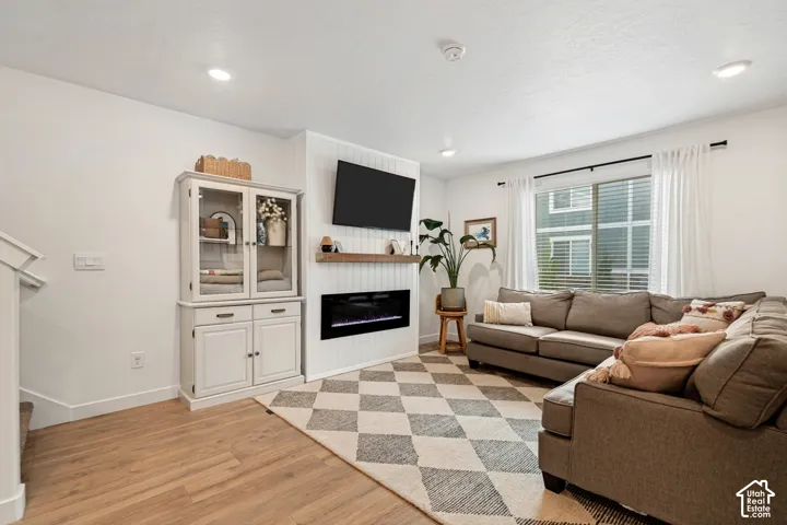 White walls, recessed lighting, wood-finish flooring, large window with blinds, and a built-in electric fireplace