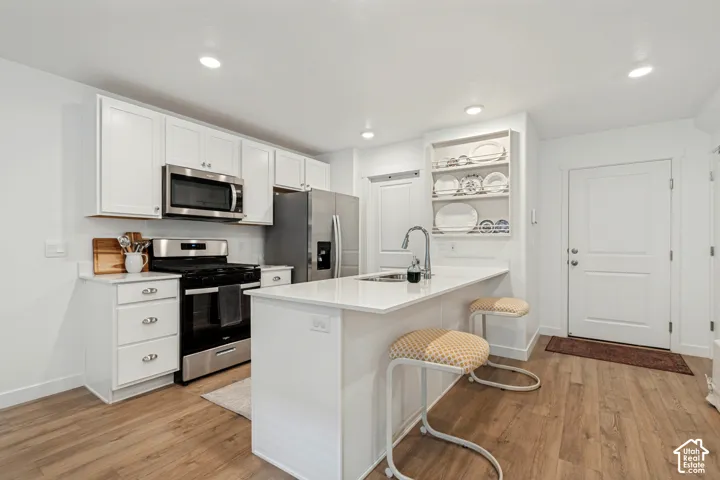 Kitchen featuring white cabinetry, stainless steel appliances, a center island with sink, white countertops, and wood-finish flooring