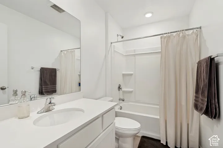 Bathroom featuring a white vanity with an integrated sink, polished chrome faucet, a large wall-mounted mirror, a white toilet, and a combined shower and bathtub with white surround
