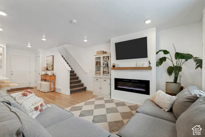 Integrated fireplace with a wood mantel, recessed lighting, wood-finish flooring, and a carpeted staircase with white railings