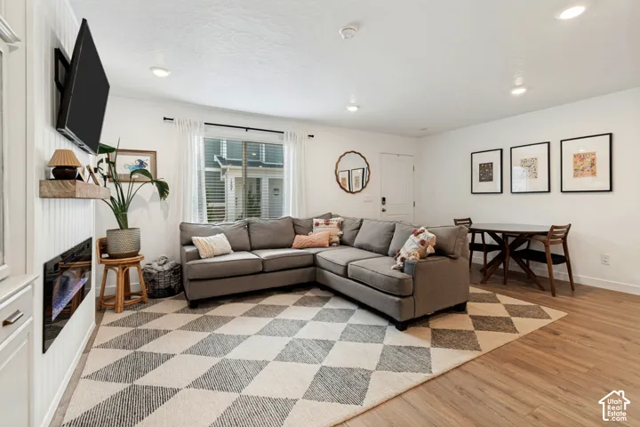Recessed lighting, wood-finish flooring, white walls, and a white paneled accent wall with a built-in electric fireplace