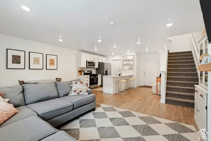 Open-concept living area featuring wood-finish flooring, recessed lighting, and a kitchen with white cabinetry and stainless steel appliances